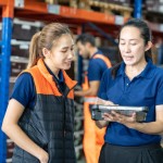 asian female manager and asian worker walking in the warehouse check product storage and doing stock counting of goods in product on pallet in warehouse by using digital tablet.
