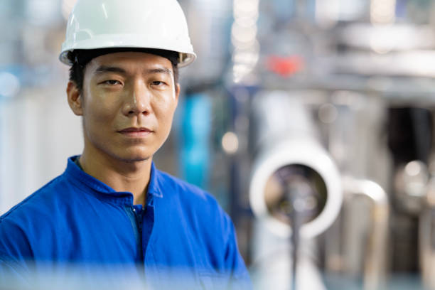 Water Treatment Systems and Management for Bottled Water Manufacturing Industry. Portrait of a Japanese Stationary Engineer working in an ingredient and filtration water storage room to examine quality in the process of water bottling.